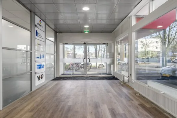 Moderne entreehal met glazen schuifdeuren, houten vloer en bedrijfsnaamborden aan de Huis-ter-Heideweg.